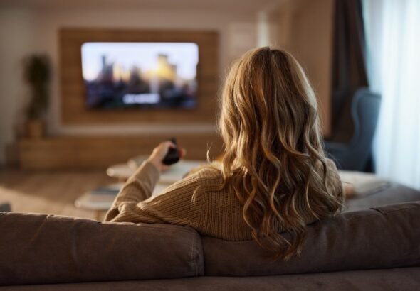 Woman relaxing on a sofa at home while choosing a TV show to watch