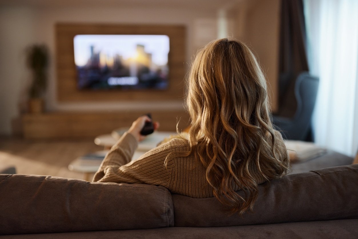 Woman relaxing on a sofa at home while choosing a TV show to watch