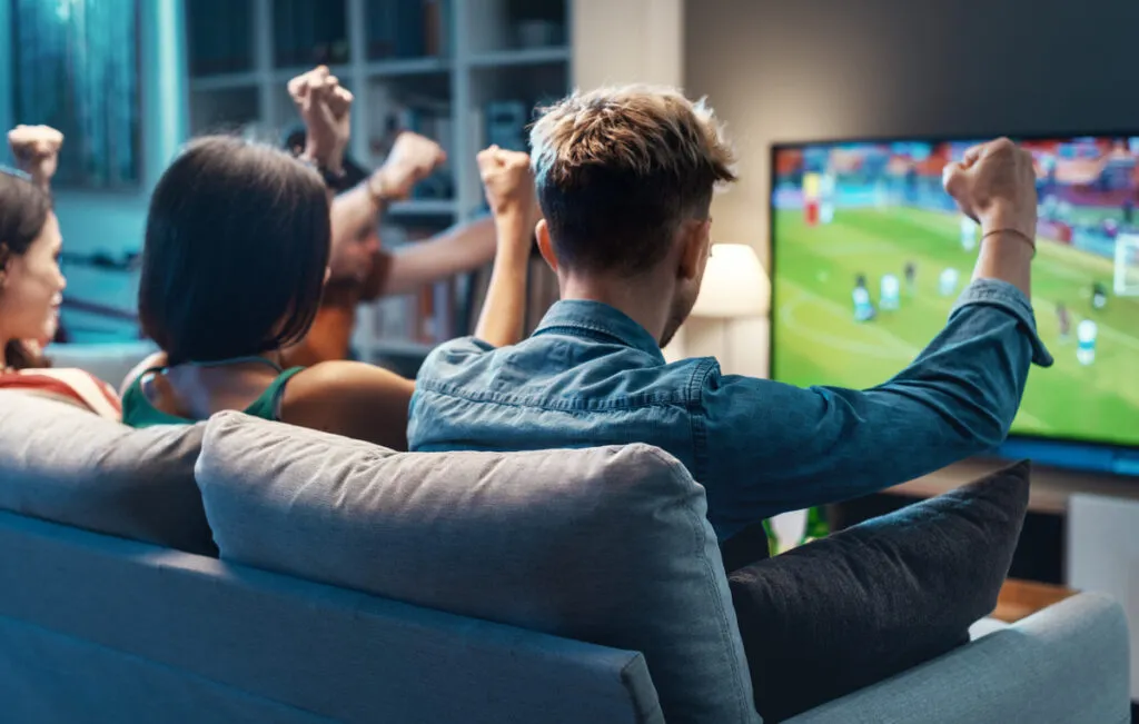 A hand holding a streaming remote pointed at a TV showing movie titles